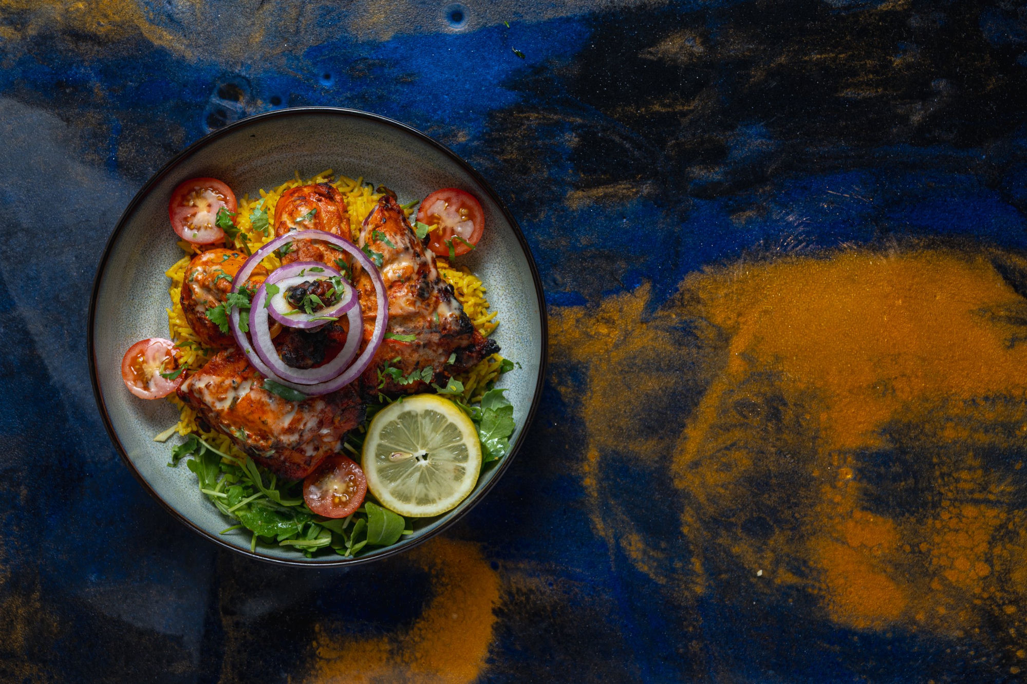 Tandoori chicken dish overhead on dramatic blue and gold surface